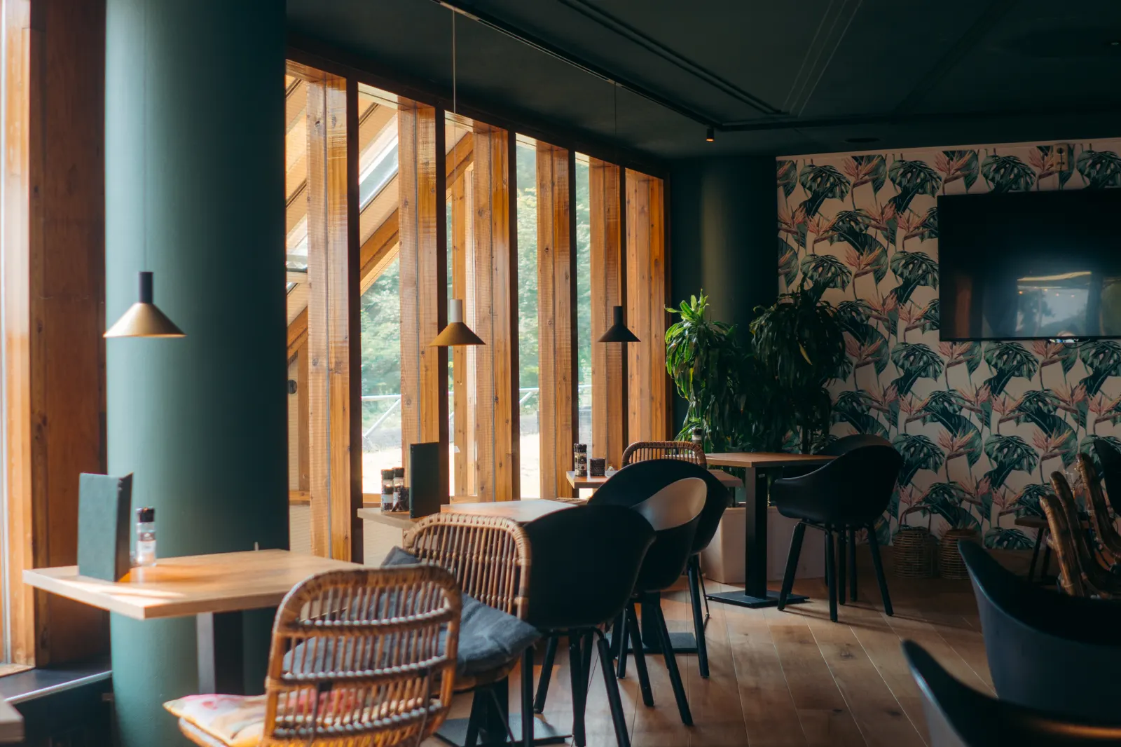 Restaurant met houten ramen, groene wanden en koperen hanglampen boven de tafels